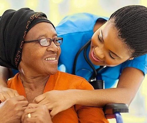 A nurse smiling as she embraces an older woman in a wheelchair