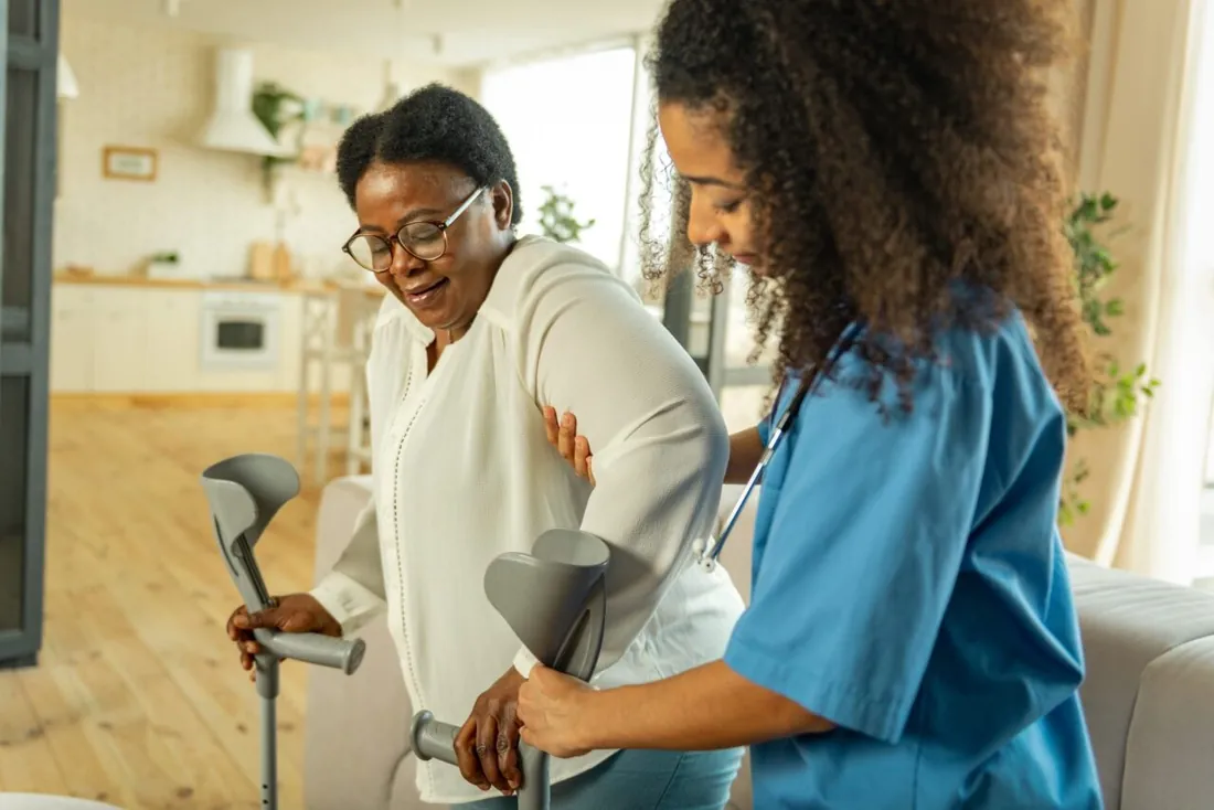 A nurse helping a woman on crutches walk safely at home